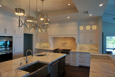 Example of a large transitional u-shaped dark wood floor and brown floor eat-in kitchen design in Jacksonville with two islands, a farmhouse sink, recessed-panel cabinets, white cabinets, marble countertops, beige backsplash, marble backsplash and stainless steel appliances