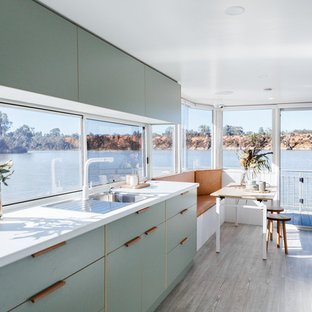 Design ideas for a beach style single-wall eat-in kitchen in Other with a drop-in sink, flat-panel cabinets, green cabinets, window splashback, panelled appliances, no island, beige floor and white benchtop.