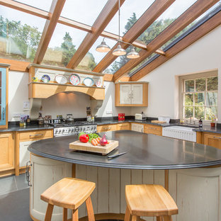 Rural l-shaped kitchen in Other with a belfast sink, shaker cabinets, medium wood cabinets, white splashback, integrated appliances, an island and grey floors.
