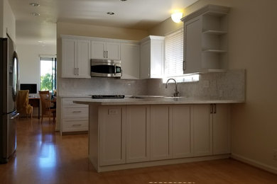 Inspiration for a medium sized classic u-shaped kitchen/diner in Hawaii with a built-in sink, flat-panel cabinets, white cabinets, quartz worktops, white splashback, stone slab splashback, stainless steel appliances, light hardwood flooring, a breakfast bar and beige floors.