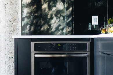 Kitchen - industrial dark wood floor kitchen idea in Minneapolis with black cabinets, quartzite countertops, mirror backsplash, stainless steel appliances, an island and white countertops
