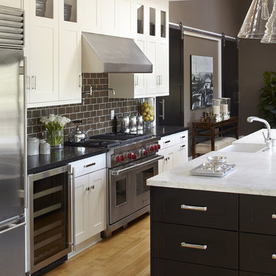 Huge transitional galley beige floor and light wood floor open concept kitchen photo in San Francisco with stainless steel appliances, subway tile backsplash, shaker cabinets, black cabinets, marble countertops, brown backsplash, a farmhouse sink, an island and white countertops