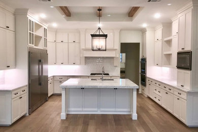 Example of a transitional u-shaped laminate floor and beige floor eat-in kitchen design in Dallas with a single-bowl sink, shaker cabinets, white cabinets, granite countertops, white backsplash, subway tile backsplash, stainless steel appliances, an island and white countertops