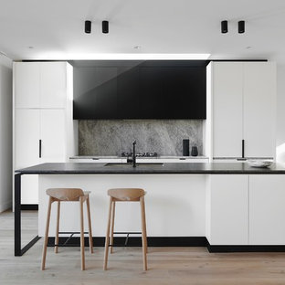 Inspiration for a contemporary galley open plan kitchen in Melbourne with an undermount sink, flat-panel cabinets, black cabinets, grey splashback, panelled appliances, light hardwood floors and with island.