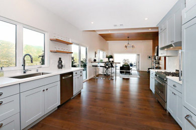 Example of a large 1960s u-shaped dark wood floor and brown floor open concept kitchen design in Los Angeles with a single-bowl sink, shaker cabinets, white cabinets, white backsplash, stainless steel appliances, no island and white countertops