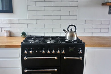 Immagine di una cucina moderna con lavello a doppia vasca, ante lisce, ante bianche, top in legno, paraspruzzi bianco, elettrodomestici neri, pavimento in legno massello medio e penisola