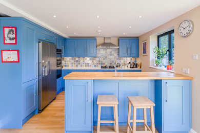 Example of a mid-sized cottage u-shaped laminate floor and beige floor eat-in kitchen design in London with an undermount sink, shaker cabinets, blue cabinets, quartz countertops, blue backsplash, mosaic tile backsplash, stainless steel appliances and a peninsula
