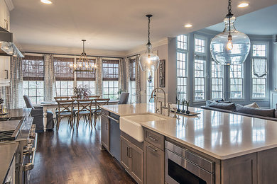 Open concept kitchen - large transitional l-shaped medium tone wood floor and brown floor open concept kitchen idea in Atlanta with a farmhouse sink, shaker cabinets, white cabinets, quartzite countertops, white backsplash, subway tile backsplash, stainless steel appliances and an island