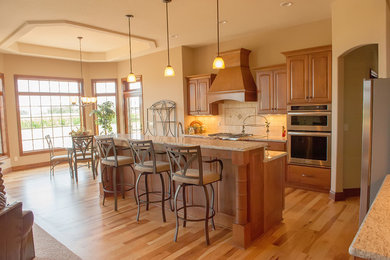 Exempel på ett mellanstort klassiskt kök, med skåp i mellenmörkt trä, granitbänkskiva, rostfria vitvaror, ljust trägolv och en köksö