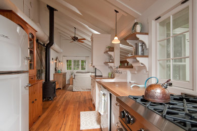 Example of a beach style galley light wood floor kitchen design in Other with shaker cabinets, white cabinets, wood countertops, a drop-in sink, white backsplash, wood backsplash and no island