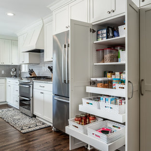Idées déco pour une cuisine américaine classique de taille moyenne avec un évier encastré, un placard à porte shaker, des portes de placard blanches, un plan de travail en granite, une crédence grise, une crédence en carrelage métro, un électroménager en acier inoxydable, un sol en bois foncé et un îlot central.