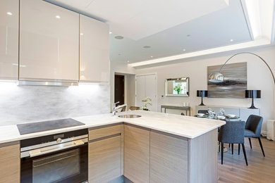 Inspiration for a small contemporary u-shaped open plan kitchen in London with flat-panel cabinets, light wood cabinets, grey splashback, black appliances, medium hardwood flooring, no island, a built-in sink and brown floors.