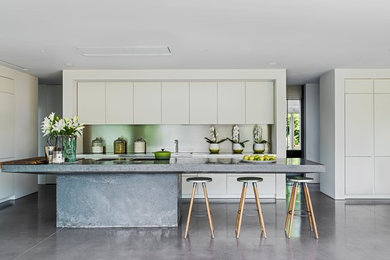 This is an example of a contemporary open plan kitchen in Berkshire with flat-panel cabinets, white cabinets, concrete worktops, metallic splashback, concrete flooring, an island, grey floors and grey worktops.