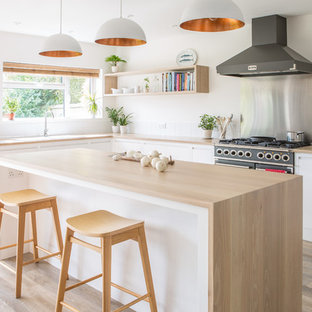 Photo of a large scandinavian l-shaped open plan kitchen in Other with a double-bowl sink, flat-panel cabinets, white cabinets, wood benchtops, white splashback, porcelain splashback, light hardwood floors and with island.