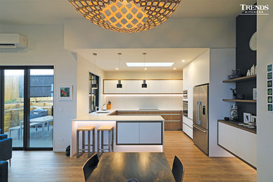 Moderne Wohnküche in L-Form mit weißen Schränken, Mineralwerkstoff-Arbeitsplatte, Küchengeräten aus Edelstahl, Laminat und weißer Arbeitsplatte in Christchurch