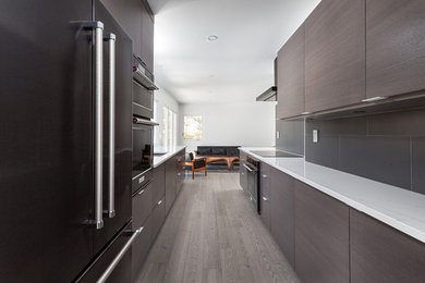 Inspiration for a mid-century modern galley light wood floor kitchen remodel in Toronto with a double-bowl sink, flat-panel cabinets, dark wood cabinets, quartz countertops, gray backsplash, porcelain backsplash, black appliances and white countertops