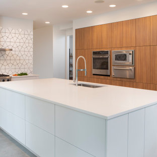 Cette image montre une grand cuisine design en L fermée avec un évier posé, un placard à porte plane, des portes de placard blanches, un plan de travail en quartz modifié, une crédence jaune, une crédence en mosaïque, un électroménager en acier inoxydable, un sol en bois brun, un îlot central, un sol marron et un plan de travail blanc.