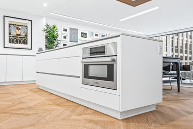 Eat-in kitchen - mid-sized modern single-wall light wood floor and brown floor eat-in kitchen idea in Chicago with an undermount sink, flat-panel cabinets, white cabinets, quartz countertops, white backsplash, stainless steel appliances, an island and white countertops