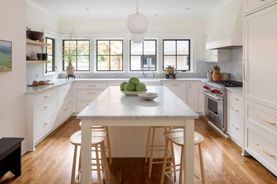 Example of a transitional u-shaped medium tone wood floor and brown floor enclosed kitchen design in Minneapolis with a farmhouse sink, shaker cabinets, white cabinets, marble countertops, gray backsplash, marble backsplash, paneled appliances, an island and gray countertops