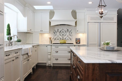Example of a classic l-shaped dark wood floor and brown floor kitchen design in Minneapolis with a farmhouse sink, recessed-panel cabinets, white cabinets, white backsplash, subway tile backsplash, paneled appliances, an island and white countertops