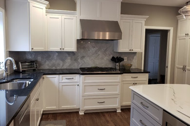 Example of a large transitional u-shaped medium tone wood floor and brown floor open concept kitchen design in Minneapolis with an undermount sink, shaker cabinets, white cabinets, quartz countertops, gray backsplash, marble backsplash, stainless steel appliances, an island and black countertops