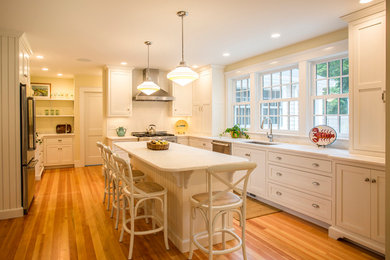 Inspiration for a large coastal l-shaped light wood floor eat-in kitchen remodel in Boston with an undermount sink, shaker cabinets, white cabinets, white backsplash, subway tile backsplash, stainless steel appliances and an island