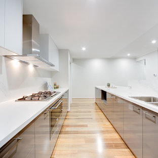 Inspiration pour une cuisine ouverte design en L avec un évier 2 bacs, un placard à porte plane, des portes de placard grises, une crédence blanche, un électroménager en acier inoxydable, un sol en bois clair et un îlot central.