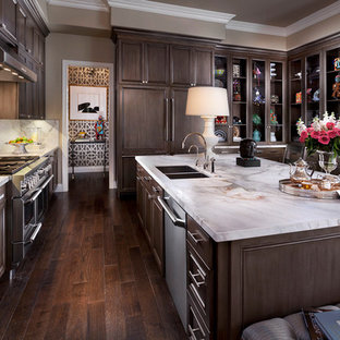 Large transitional u-shaped dark wood floor and brown floor eat-in kitchen photo in Las Vegas with a double-bowl sink, dark wood cabinets, white backsplash, stainless steel appliances, marble countertops, stone slab backsplash, an island and recessed-panel cabinets