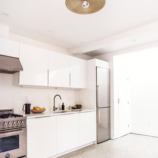 Mid-sized modern eat-in kitchen designs - Example of a mid-sized minimalist single-wall concrete floor eat-in kitchen design in San Francisco with a double-bowl sink, flat-panel cabinets, white cabinets, solid surface countertops, white backsplash, stainless steel appliances and no island