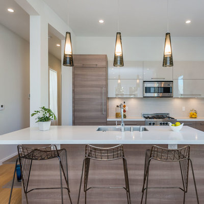 Example of a trendy galley light wood floor kitchen design in San Francisco with an undermount sink, flat-panel cabinets, medium tone wood cabinets, gray backsplash, glass sheet backsplash, stainless steel appliances and an island