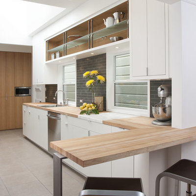 Example of a minimalist kitchen design in San Francisco with flat-panel cabinets, stainless steel appliances, wood countertops, white cabinets, gray backsplash and subway tile backsplash