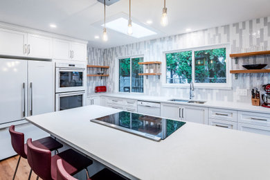 Inspiration for a mid-sized transitional l-shaped light wood floor and brown floor eat-in kitchen remodel in Vancouver with an undermount sink, shaker cabinets, white cabinets, quartzite countertops, gray backsplash, porcelain backsplash, white appliances, an island and white countertops