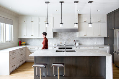 Inspiration for a transitional l-shaped light wood floor kitchen remodel in Calgary with a double-bowl sink, shaker cabinets, white cabinets, stone slab backsplash, stainless steel appliances, an island and white countertops