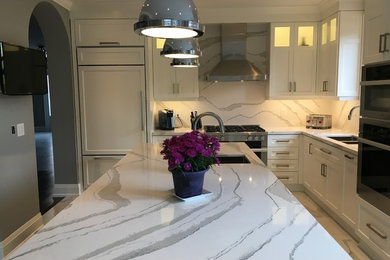 Inspiration for a large transitional l-shaped porcelain tile and white floor enclosed kitchen remodel in Toronto with an undermount sink, shaker cabinets, white cabinets, quartz countertops, white backsplash, stone slab backsplash, stainless steel appliances, an island and white countertops