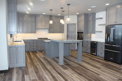 Large transitional u-shaped brown floor and medium tone wood floor kitchen photo in Other with an undermount sink, recessed-panel cabinets, gray cabinets, granite countertops, white backsplash, subway tile backsplash, an island and stainless steel appliances