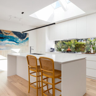 Inspiration for a mid-sized contemporary galley open plan kitchen in Melbourne with an undermount sink, flat-panel cabinets, white cabinets, quartz benchtops, window splashback, stainless steel appliances, light hardwood floors, with island, beige floor and white benchtop.