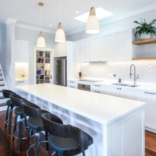 Design ideas for a large transitional galley open plan kitchen in Sydney with an undermount sink, shaker cabinets, white cabinets, solid surface benchtops, beige splashback, porcelain splashback, stainless steel appliances, dark hardwood floors, with island, brown floor and white benchtop.