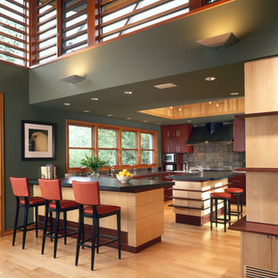 Large country u-shaped kitchen in Denver with slate splashback, an undermount sink, flat-panel cabinets, red cabinets, soapstone benchtops, grey splashback, light hardwood floors, with island and black benchtop.