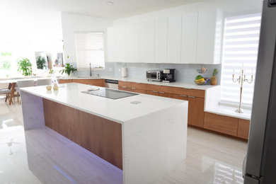 Large trendy porcelain tile and gray floor eat-in kitchen photo in Miami with a single-bowl sink, flat-panel cabinets, white cabinets, quartzite countertops, gray backsplash, glass tile backsplash, stainless steel appliances, an island and white countertops