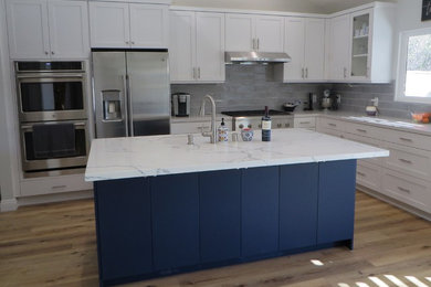 Example of a mid-sized transitional l-shaped laminate floor eat-in kitchen design in Orange County with shaker cabinets, white cabinets, quartz countertops, gray backsplash, subway tile backsplash, stainless steel appliances, an island and white countertops