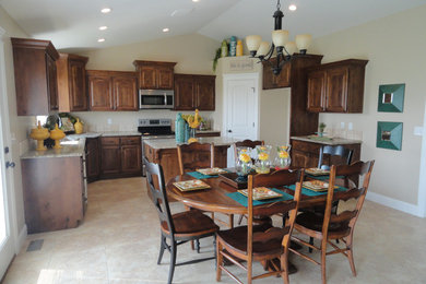 Example of a large classic l-shaped terra-cotta tile eat-in kitchen design in Boise with a double-bowl sink, raised-panel cabinets, medium tone wood cabinets, granite countertops, beige backsplash, stone tile backsplash, stainless steel appliances and an island