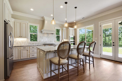Example of a mid-sized transitional medium tone wood floor and brown floor enclosed kitchen design in New Orleans with an island, beaded inset cabinets, beige cabinets, marble countertops, gray backsplash, marble backsplash, stainless steel appliances and gray countertops