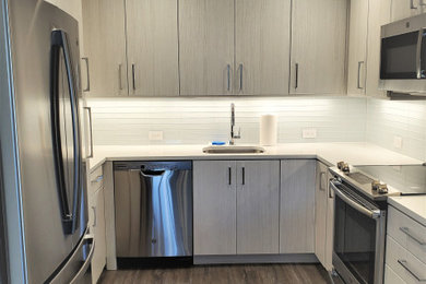 Photo of a small modern u-shaped enclosed kitchen in Philadelphia with a submerged sink, flat-panel cabinets, grey cabinets, engineered stone countertops, white splashback, glass tiled splashback, stainless steel appliances, vinyl flooring, no island, brown floors and white worktops.