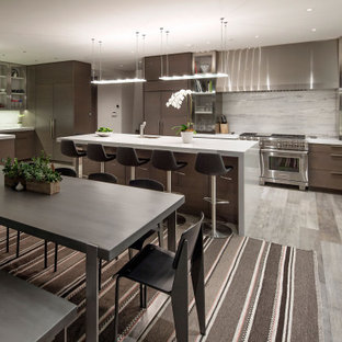 Modelo de cocina comedor en U, moderna, grande, con fregadero bajoencimera, armarios con paneles lisos, puertas de armario marrones, salpicadero blanco, electrodomésticos de acero inoxidable, suelo laminado, una isla, suelo gris y encimeras blancas
