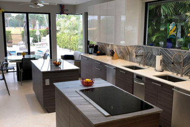 Example of a large minimalist galley limestone floor and beige floor enclosed kitchen design in Miami with an undermount sink, flat-panel cabinets, porcelain backsplash, stainless steel appliances and two islands