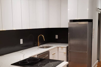 Example of a mid-sized minimalist u-shaped open concept kitchen design in Philadelphia with a single-bowl sink, flat-panel cabinets, white cabinets, quartz countertops, black backsplash, stainless steel appliances and white countertops