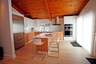 Mid-sized minimalist l-shaped laminate floor eat-in kitchen photo in Portland Maine with flat-panel cabinets, stainless steel appliances, an island, an undermount sink, light wood cabinets and quartz countertops