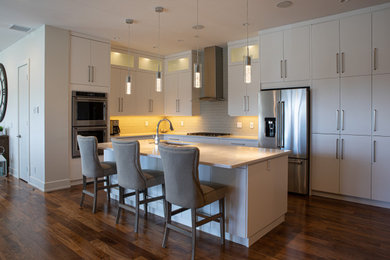 Example of a large transitional l-shaped dark wood floor and brown floor eat-in kitchen design in Edmonton with a double-bowl sink, flat-panel cabinets, white cabinets, quartz countertops, gray backsplash, glass tile backsplash, stainless steel appliances, an island and white countertops