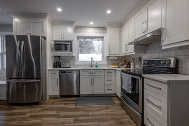 Example of a mid-sized trendy l-shaped vinyl floor, brown floor and coffered ceiling eat-in kitchen design in Montreal with a single-bowl sink, shaker cabinets, white cabinets, quartz countertops, white backsplash, ceramic backsplash, stainless steel appliances, no island and white countertops