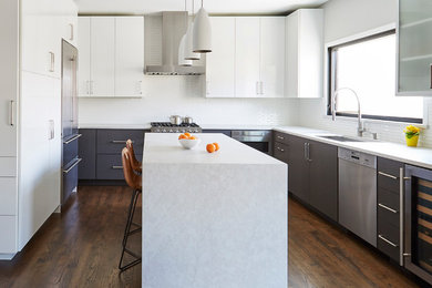 This is an example of a contemporary u-shaped kitchen in Chicago with a submerged sink, flat-panel cabinets, grey cabinets, white splashback, stainless steel appliances, dark hardwood flooring, an island, brown floors and white worktops.